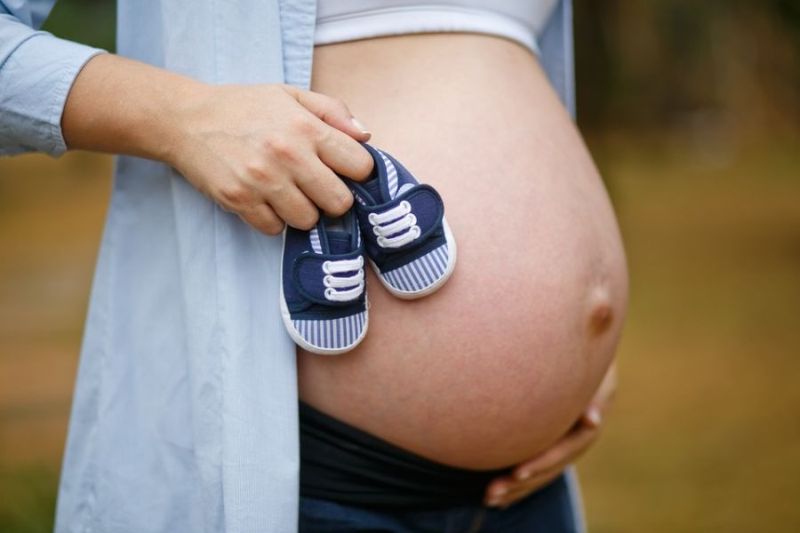 Nahé břicho těhotné ženy s dětskými botičkami