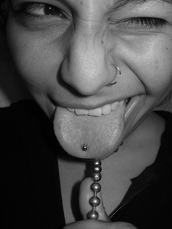 Dívka vyplazující jazyk s piercingem v jazyku a nose